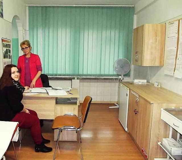 W gabinecie lekarskim pielęgniarka stoi przy biurku. Na krześle siedzi uczennica 