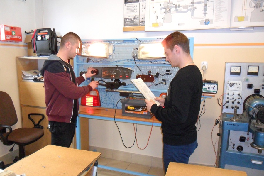 dwóch uczniów stoi przy tablicy symulująca schemat instalacji elektrycznej w samochodzie