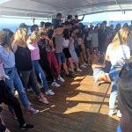 Na pokładzie statku grupa osób tańczy Zorbę