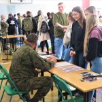 Uczniowie podchodzą do stolika przy, którym siedzi żołnierz