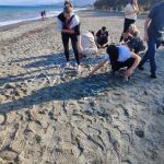 Uczniowie układają napis z kamieni na plaży.