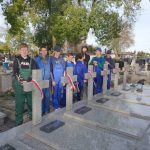 Grupa uczniów w strojach roboczych stoi przy grobach