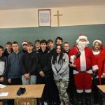 Uczeń w stroju Świętego Mikołaja wraz z grupą uczniów i nauczycielem pozują do zdjęcia.
