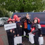 Grupka dzieci uczestniczących w zawodach strażackich. Trzymają w rękach puchar i nagrody.