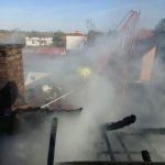 Nadpalona część dachu budynku. Dwóch strażaków na zwyżce dogaszają pożar.