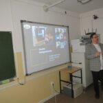 Nauczyciel stoi przy ekranie z wyświetlanym fragmentem prezentacji