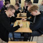 Uczniowie siedzą przy stolikach i grają w szachy