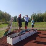 Na podium stoją trzy udekorowane medalami dziewczyny.