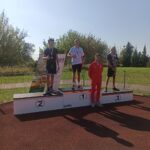 Dekoracja chłopców. Na podium stoi trzech udekorowanych medalami chłopców.